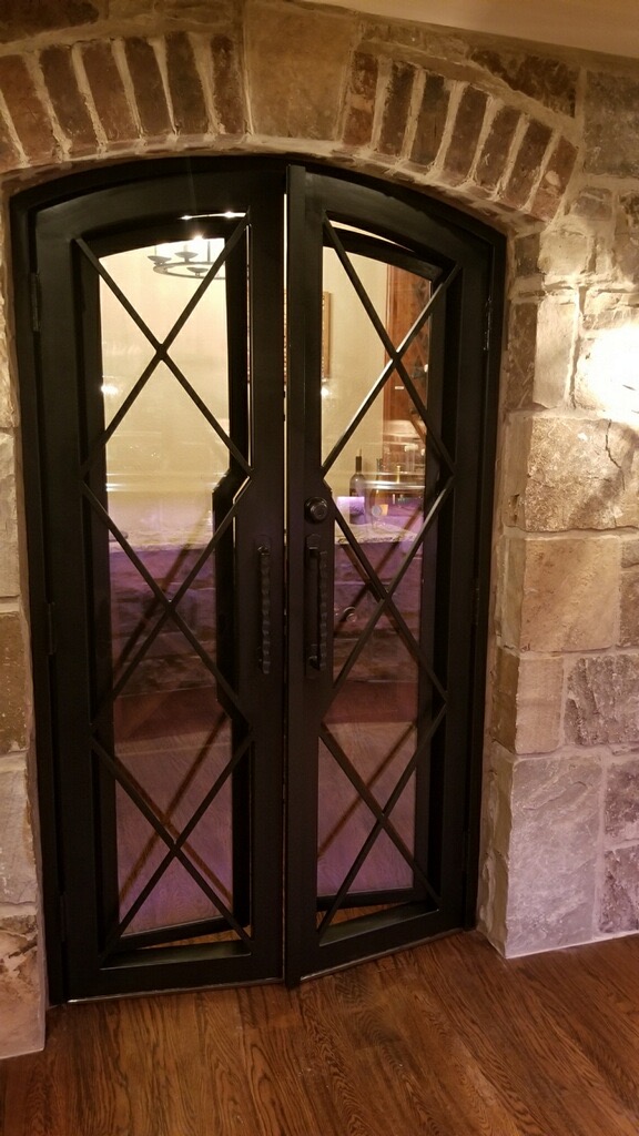 A custom semi arched wine cellar door in an Atlanta basement installed between stone and brick